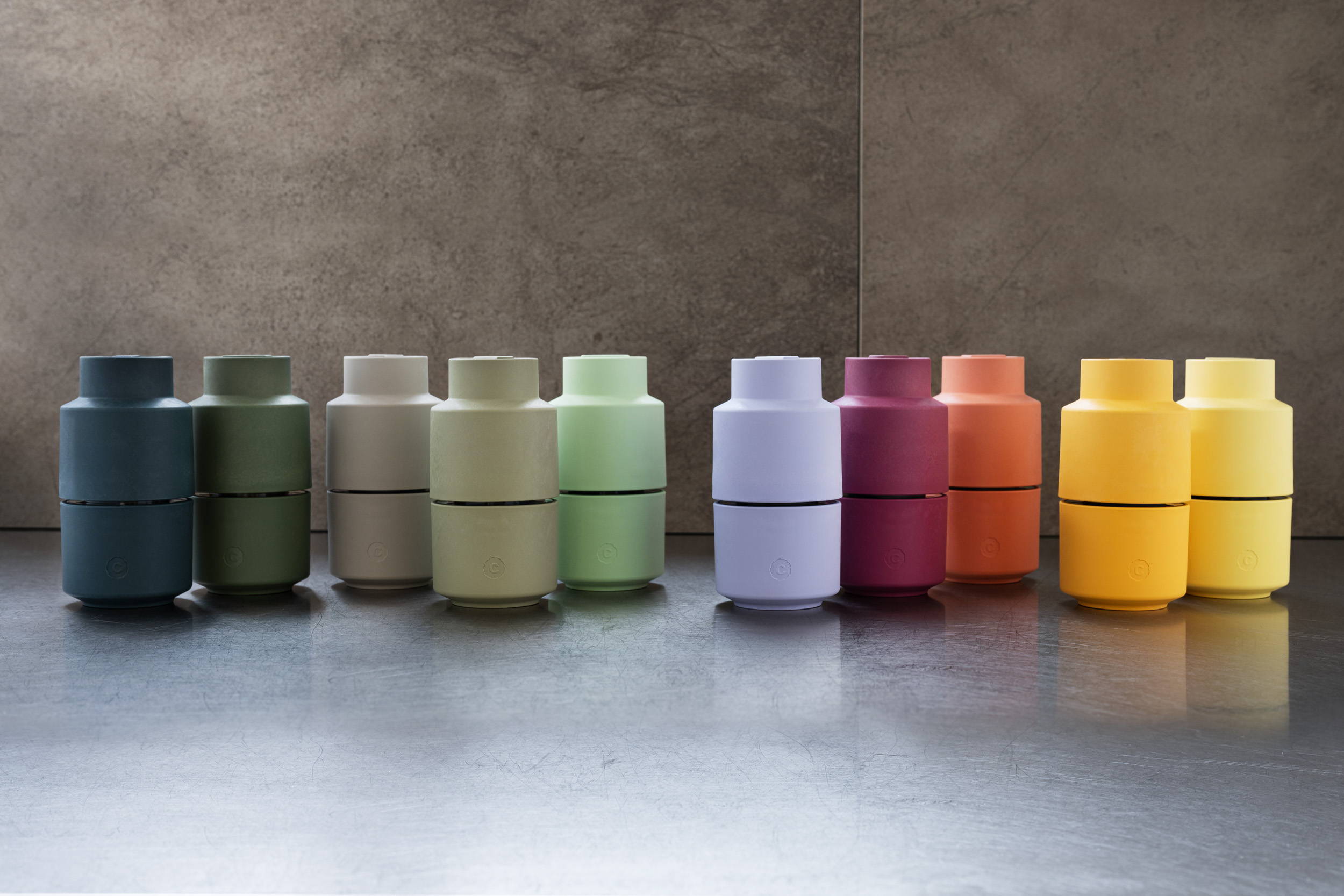 Ten colorful pepper grinders in pairs, arranged left to right on a metallic surface under neutral wall.