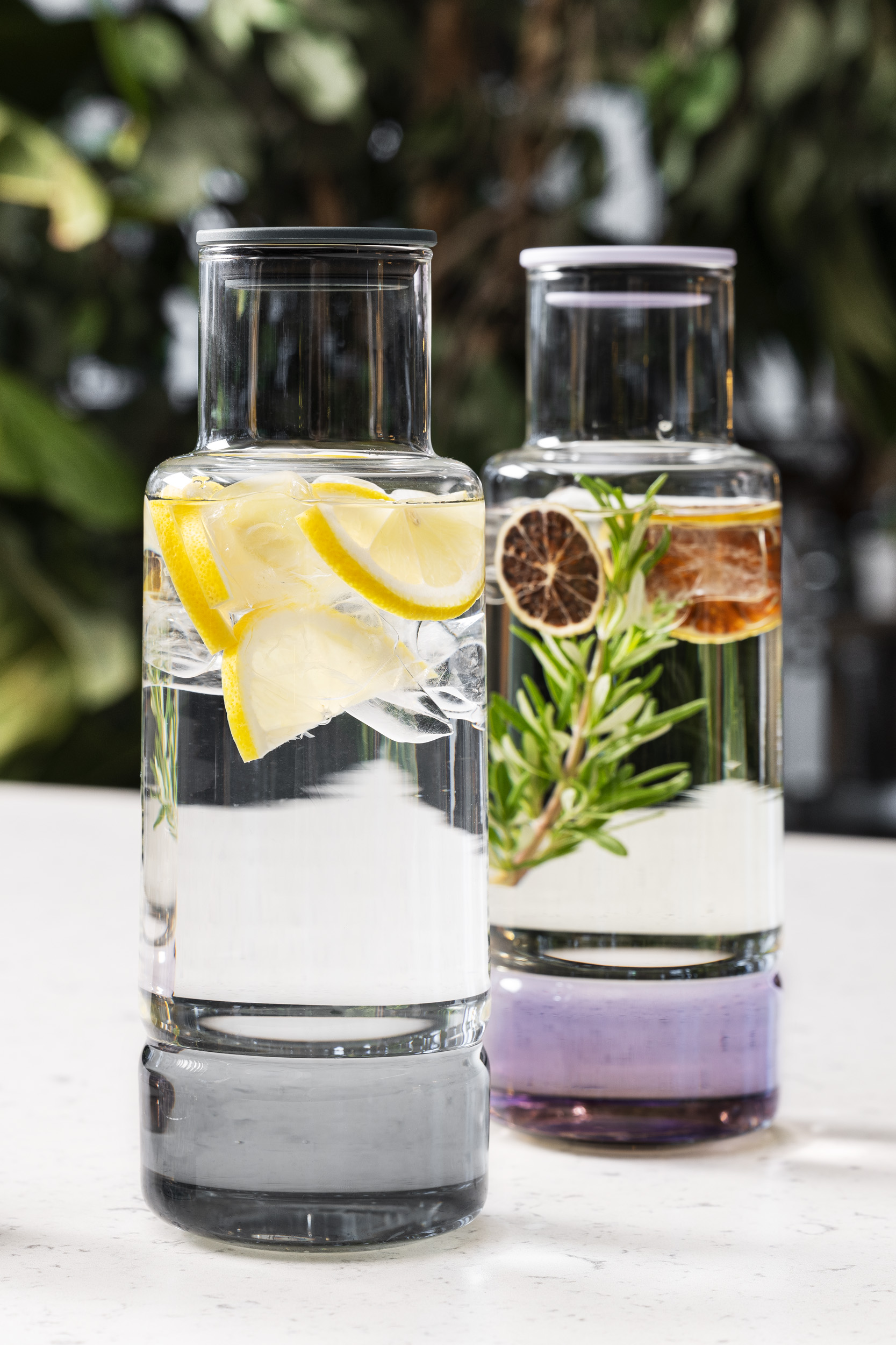 Two glass pitchers with infused water: one with lemon and ice, the other with herbs and dried citrus.